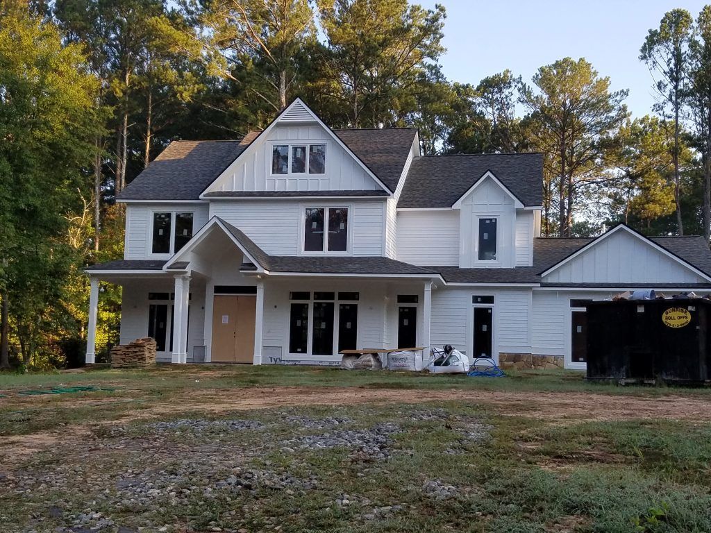 A large white house is being built in a field surrounded by trees.